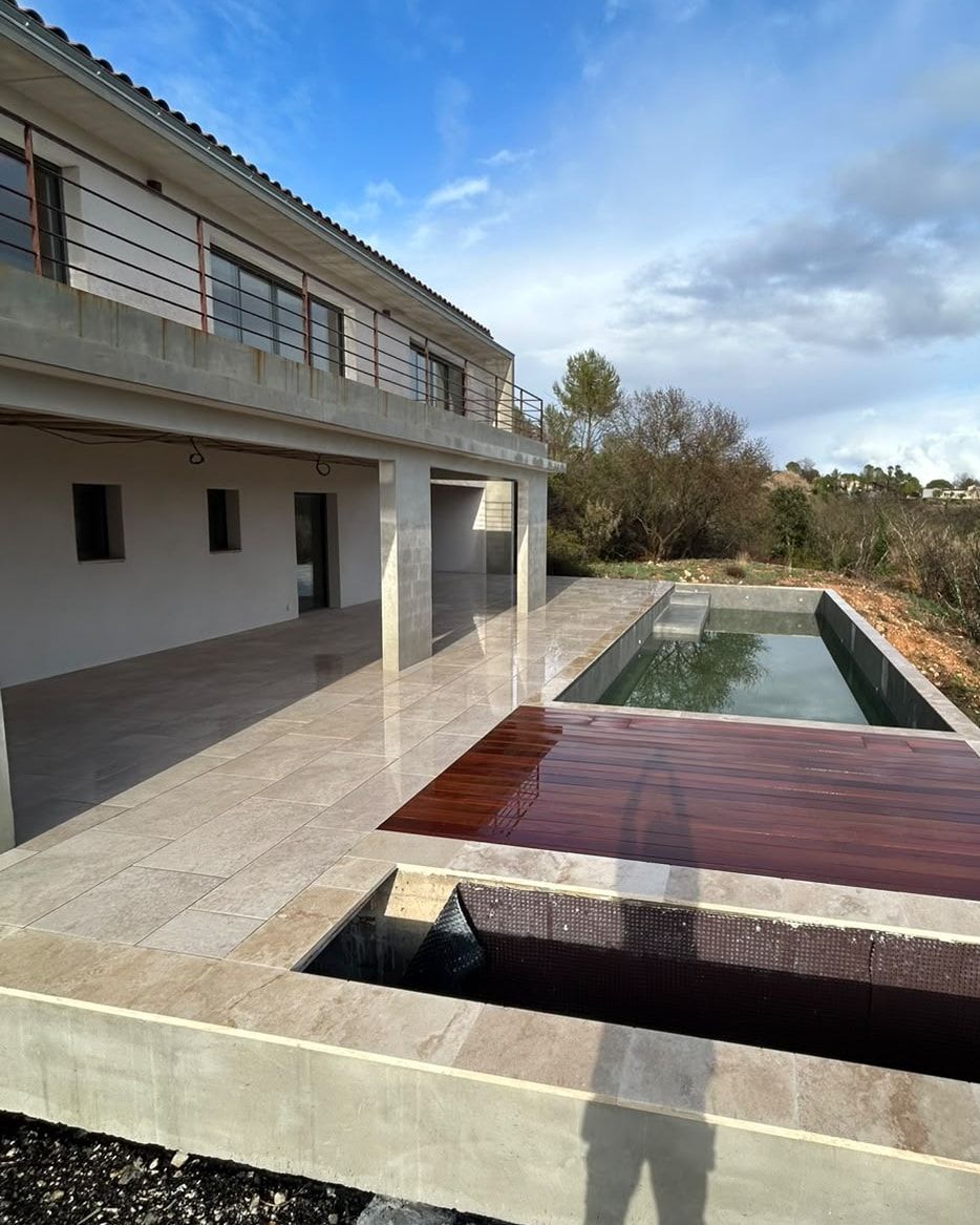 Vue d’ensemble d’une villa contemporaine à Combaillaux, avec terrasse couverte, bassin et terrasse en bois dans un paysage de garrigue